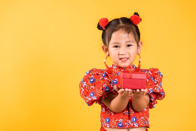 Szczęśliwa azjatycka chińska dziewczynka uśmiech nosi czerwone cheongsam trzyma pudełko na prezent
