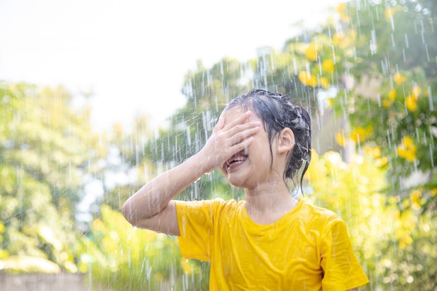 Szczęśliwa Azjatycka dziewczynka bawi się z deszczem w słońcu