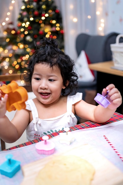 Szczęśliwa Azjatycka dziewczynka gotowanie piernika w domu z rodzicem na Boże Narodzenie. Domowe ciasteczka świąteczne dla dziecka.