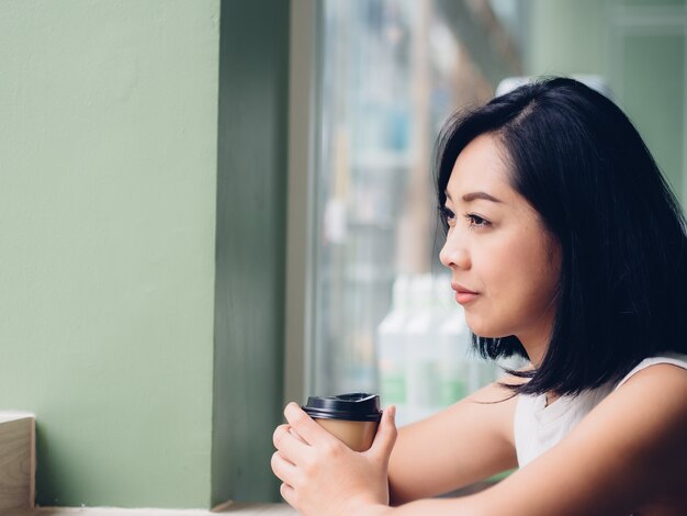 Szczęśliwa Azjatycka kobieta pije gorącą filiżankę kawy w pokojowej atmosferze