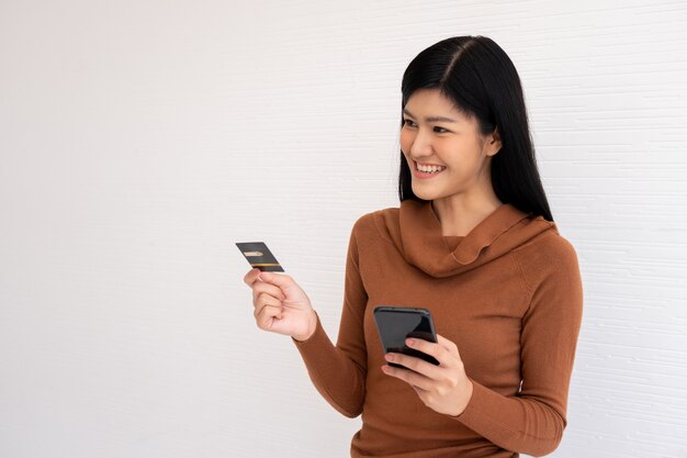 Szczęśliwa Azjatycka kobieta trzyma kartę kredytową i smartphone dla bankowości mobilnej w Internecie.
