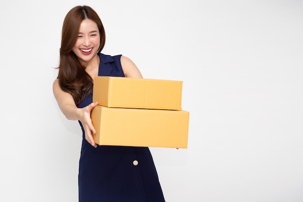 Szczęśliwa Azjatycka kobieta uśmiecha się i trzyma pudełko paczek na białym tle na jasnozielonej ścianie.