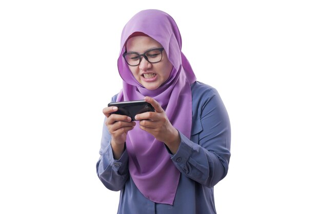 Szczęśliwa azjatycka muzułmańska kobieta podekscytowana grą w gry na swoim smartfonie odizolowana na białym