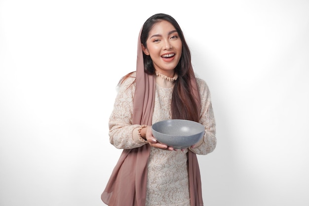 Szczęśliwa azjatycka muzułmańska kobieta trzymająca miskę i sztućce do jedzenia po postu, uśmiechając się radośnie na izolowanym białym tle koncepcja Ramadanu