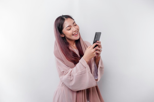 Szczęśliwa azjatycka muzułmańska kobieta w chustce trzymająca telefon odizolowany białym tłem