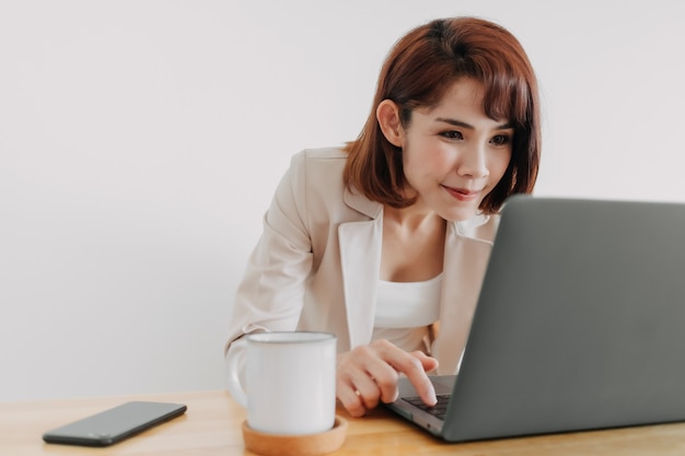 Szczęśliwa azjatycka pracująca kobieta pracuje na swoim laptopie w biurze