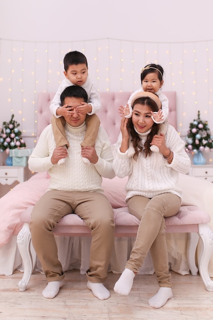 Szczęśliwa azjatycka rodzina z dwójką dzieci w przytulnych wygodnych swetrach, bawiąc się i relaksując na łóżku