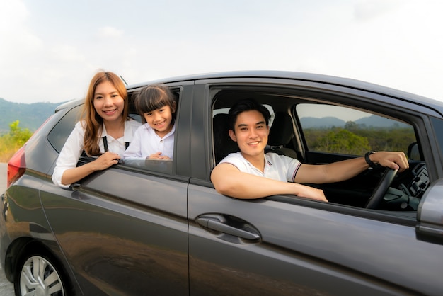 Szczęśliwa Azjatycka rodzina z ojcem, matką i córką w kompaktowym samochodzie jest uśmiechnięta i jedzie w podróż na wakacje.
