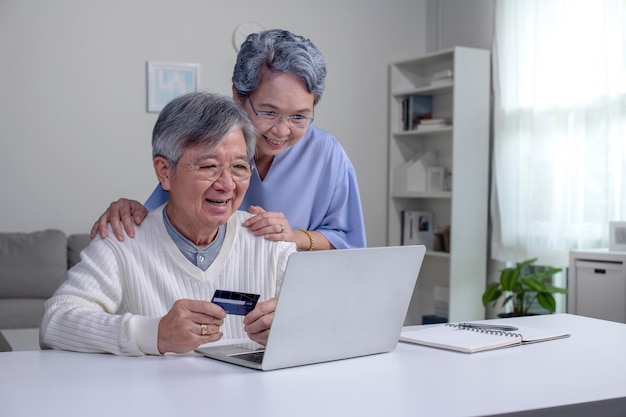 Szczęśliwa azjatycka starsza para w domu Przystojny staruszek i atrakcyjna stara kobieta spędzają razem czas Starsza para z laptopem i kartą kredytową w rękach Zakupy online