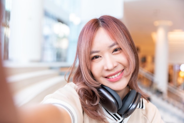 Szczęśliwa azjatycka studentka słucha muzyki na słuchawkach w bibliotece kampusu na uniwersytecie