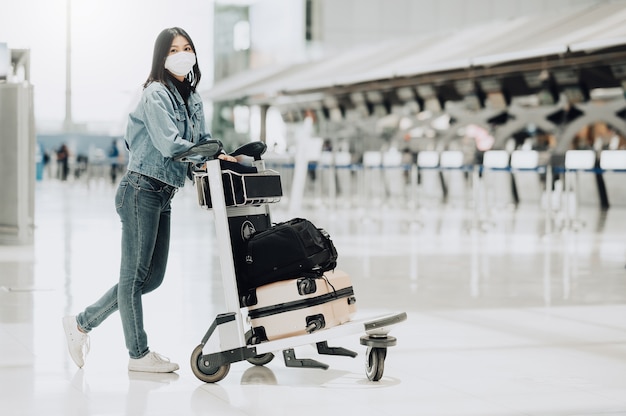 Szczęśliwa Azjatycka turystka kobieta z maską spaceru z wózkiem na bagaż