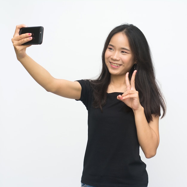 Szczęśliwa azjatykcia młoda dziewczyna wskazuje dwa palca i bierze selfie