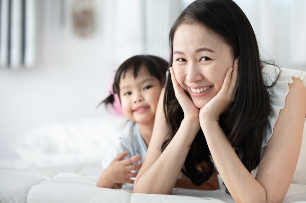 Szczęśliwa azjatykcia rodziny matka z córką bawić się na łóżku z uśmiech twarzą