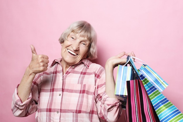 Szczęśliwa babcia z torbami na zakupy na różowym tle Koncepcja stylu życia i ludzi