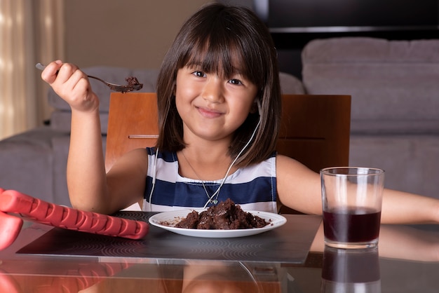 Szczęśliwa bardzo mała dziewczynka oglądając tablet i jedzenie ciasta czekoladowego