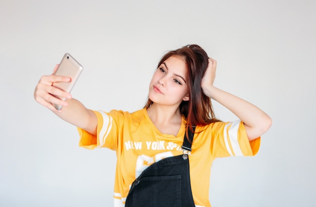 Szczęśliwa beztroska uśmiechnięta nastolatek dziewczyna z ciemnymi długimi włosami w żółtej koszulce robi selfie