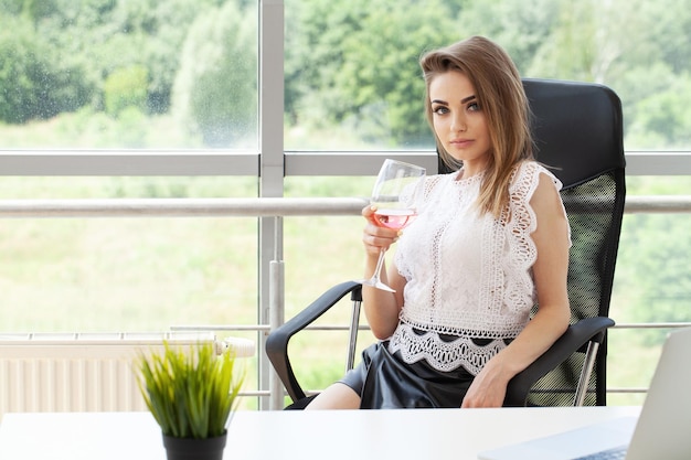 Szczęśliwa biznesowa kobieta opiekająca kieliszek wina w biurze i patrząca na kamerę