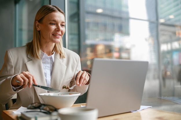 Szczęśliwa bizneswoman ma biznesowy lunch i pracuje na laptopie w kawiarni zamazanym tle