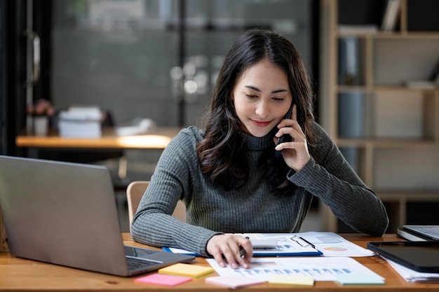 Szczęśliwa bizneswoman rozmawiająca przez telefon komórkowy podczas analizowania wykresu biznesowego na biurku