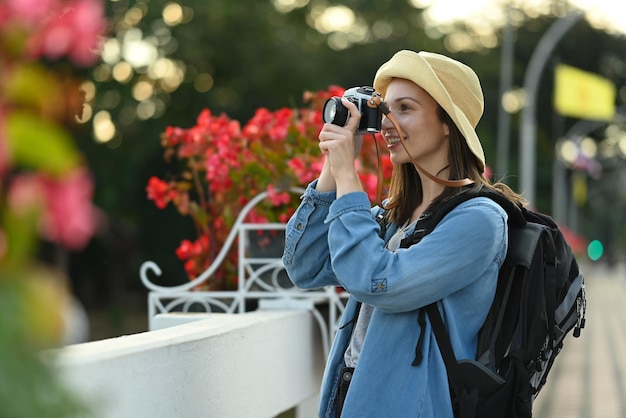 Szczęśliwa blogerka podróżnicza z plecakiem robiąca zdjęcie na moście z pięknym kwitnącym tłem kwiatów