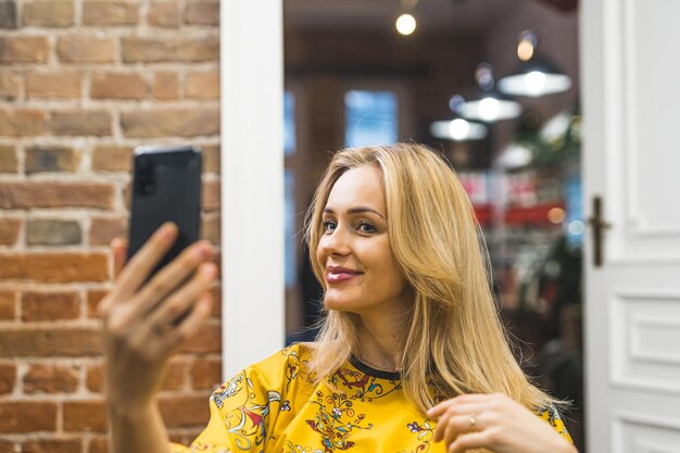 Szczęśliwa blond klientka z stylizowanymi włosami patrząca na telefon po średnim zbliżeniu fryzury