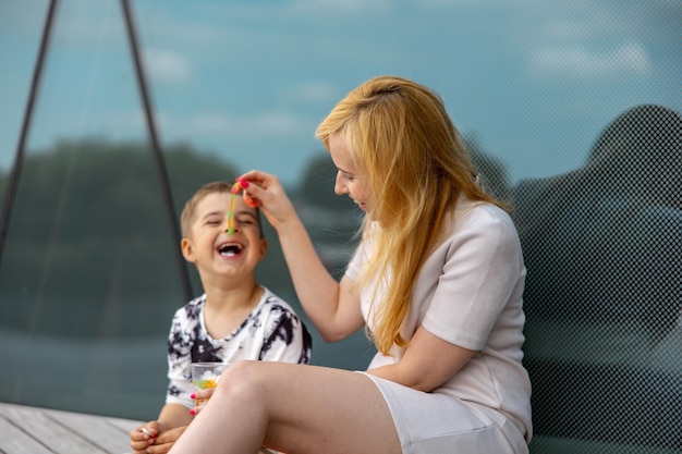 Szczęśliwa blond kobieta i mały chłopiec siedzą na tarasie i jedzą słodycze Matka i syn cieszą się razem Pozytywna młoda mama bawi się, spędzając czas ze swoim słodkim dzieckiem, śmiejąc się, bawiąc się Rodzina