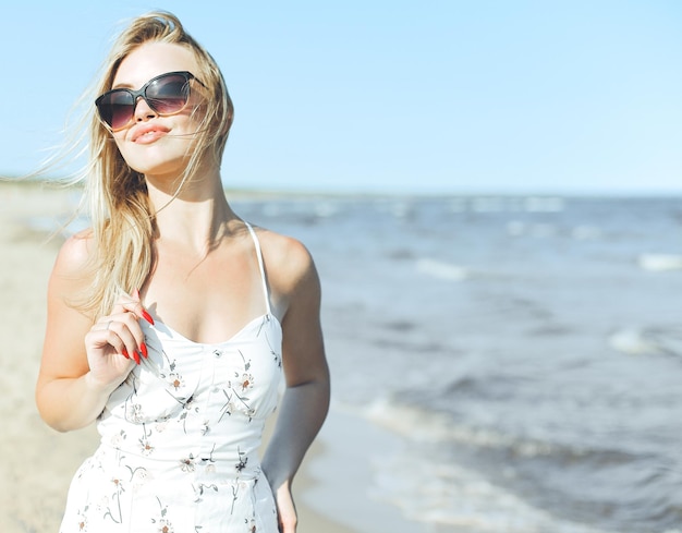 Szczęśliwa blondynka w błogości wolnego szczęścia na plaży oceanu stojąca w okularach przeciwsłonecznych