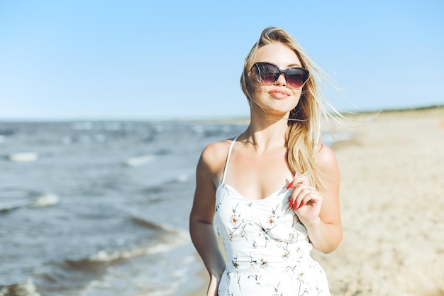 Szczęśliwa blondynka w błogości wolnego szczęścia na plaży oceanu stojąca w okularach przeciwsłonecznych.