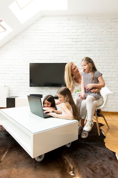 Szczęśliwa blondynki matka z jej córkami używa laptop w domu w żywym pokoju