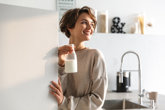 Szczęśliwa brunetka kobieta pije mleko i odwracając stojąc w kuchni