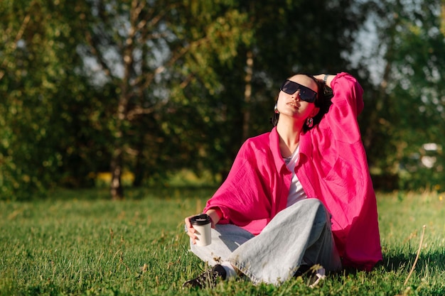 Szczęśliwa brunetka kobieta w zwykłych ubraniach, siedząca na trawniku i odpoczywająca w parku w słoneczny dzień