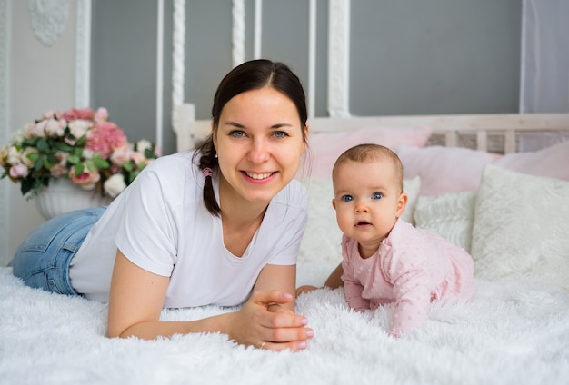 Szczęśliwa brunetka mama z córką leży na łóżku w pokoju i patrzy w kamerę