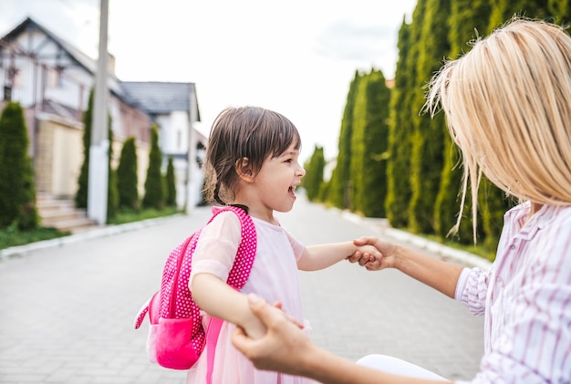 Szczęśliwa córka mała dziewczynka i ładna mama przytulają się na chodniku na ulicy Mama spotkała dziecko po przedszkolu w domu na zewnątrz Mama i dziecko bawią się Koncepcja dnia matki