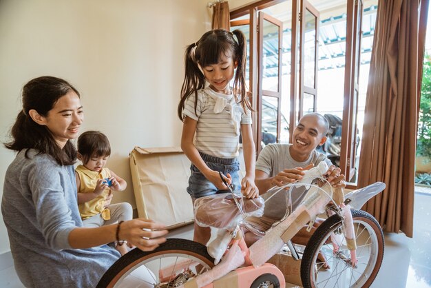 Szczęśliwa córka tnie plastikową folię, trzymając nowy mini rower