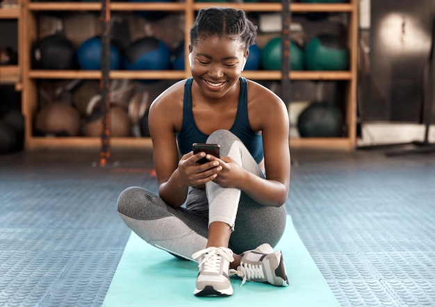 Szczęśliwa czarna kobieta fitness i telefon do komunikacji w mediach społecznościowych lub sieci na siłowni Afrykańska kobieta lub sportowiec pisze SMS-y lub rozmawia na smartfonie po treningu