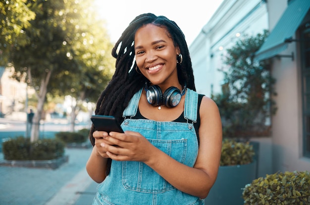 Szczęśliwa czarna kobieta w mieście w rozmowie na smartfonie i SMS-ach w mediach społecznościowych Spacerująca po ulicy miejska czarna dziewczyna uśmiecha się i ze szczęścia korzysta z połączenia 5g do komunikacji mobilnej