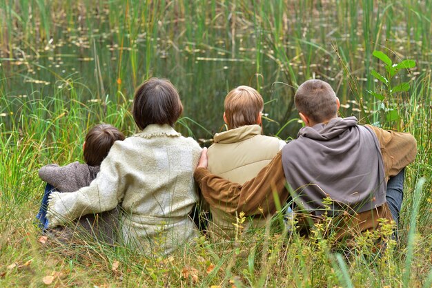 Szczęśliwa czteroosobowa rodzina siedzi razem w parku jesienią i patrzy na staw