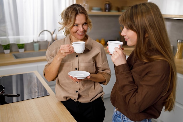 Szczęśliwa dojrzała kobieta delektująca się kawą z dorosłą córką w kuchni