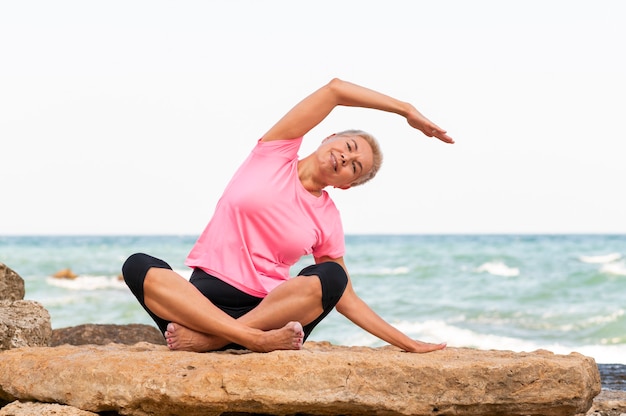 Zdjęcie szczęśliwa dojrzała kobieta nad morzem robić ćwiczenia jogi