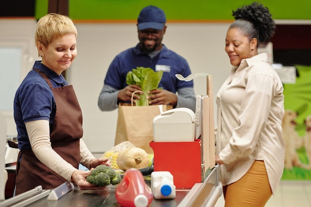 Szczęśliwa dojrzała sprzedawczyni stojąca przy kasie w supermarkecie