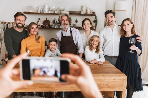 Szczęśliwa Duża Rodzina Pozuje Do Aparatu Fotograficznego, Stojąc Przy Kuchennym Stole I świętując Wigilię