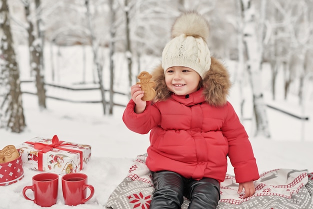 Szczęśliwa dziecko dziewczyna na zima spacerze outdoors pije herbaty. uśmiechnięte dziecko małe dziecko grając w zimowe Święta Bożego Narodzenia. Święta Rodzina w winter park. Dziewczyna w zimowym lesie.