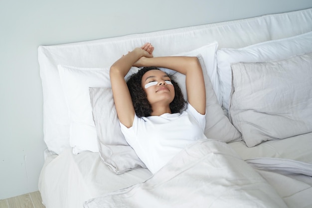 Szczęśliwa dziewczyna afro śpi z opaskami na oczy Młoda kobieta relaksuje się w domu w weekendowy poranek w łóżku
