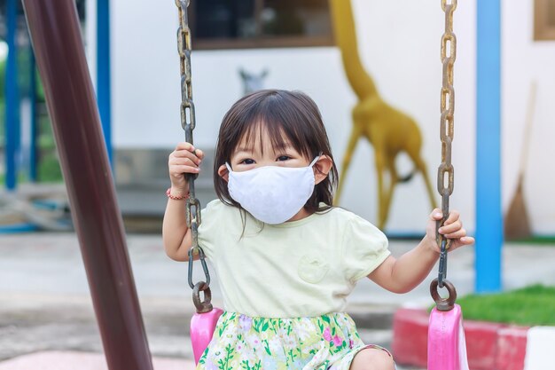 Szczęśliwa Dziewczyna Azjatyckich Dziecko Sobie Maskę Z Tkaniny. Bawi Się Na Placu Zabaw.