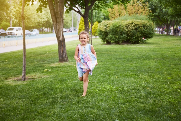 Szczęśliwa dziewczyna biegnie przez trawę w kolorowej sukience. Gra w parku. Ciesz się latem