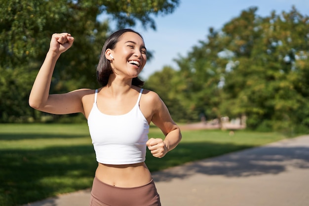 Szczęśliwa dziewczyna fitness osiąga cel ukończenia maratonu biegając z rękami do góry świętując zwycięstwo podczas jogg