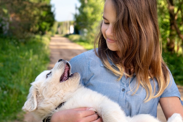 Szczęśliwa dziewczyna gra z cute puppy pirenejskiego psa górskiego, trzymając go na rękach w letni dzień na świeżym powietrzu