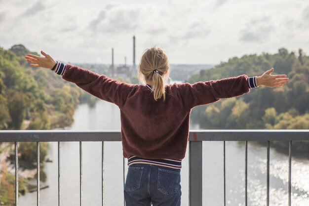 Zdjęcie szczęśliwa dziewczyna na moście, czująca się wolna i patrząca na niebieską rzekę