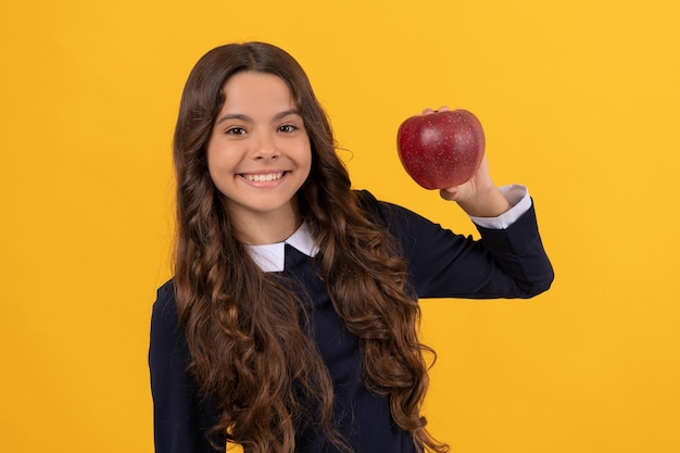 Szczęśliwa dziewczyna pokazuje czerwone jabłko witaminy na obiad na żółtym tle, witamina.