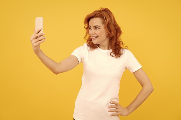 Szczęśliwa dziewczyna uśmiecha się do telefonu z aparatem komórkowym na żółtym tle wideo selfie